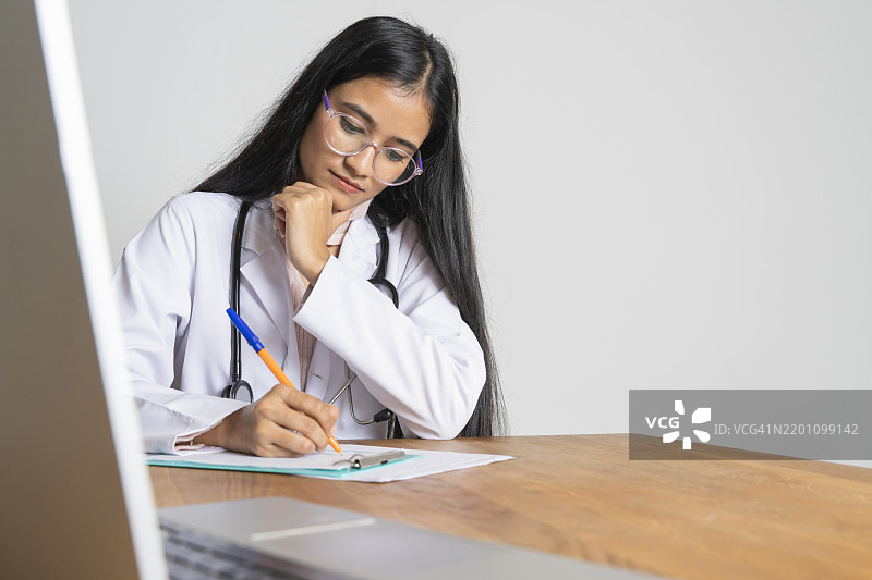 年轻医生坐在桌旁开处方，正在诊所工作图片素材
