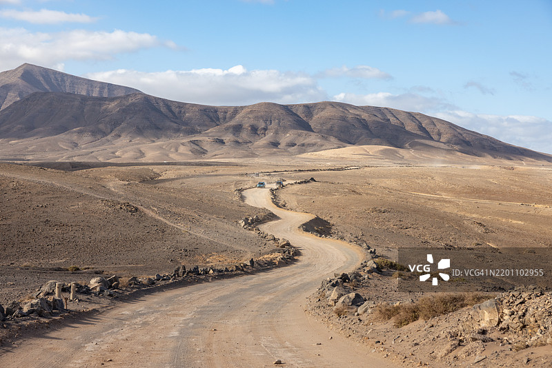 在西班牙兰萨罗特的白沙滩，蜿蜒的碎石路穿过干旱的沙漠景观图片素材