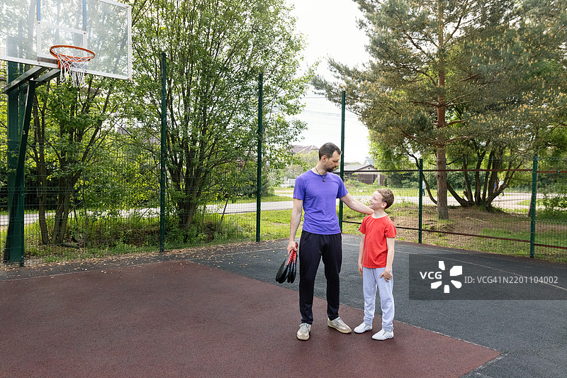 父亲和儿子在户外篮球场分享快乐时光。在春季训练中教导和增进感情。图片素材