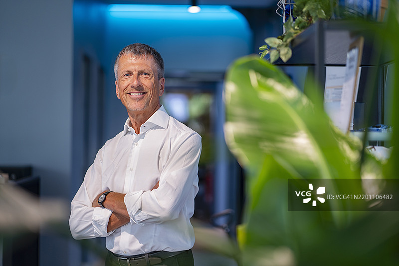 快乐的高级商务人士双臂交叉站在办公室里图片素材