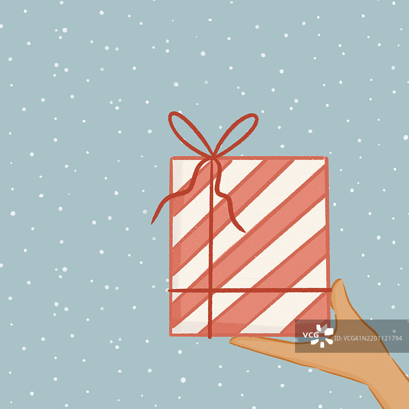 在雪花飘落的圣诞场景中，手握着一个包裹好的礼物图片素材
