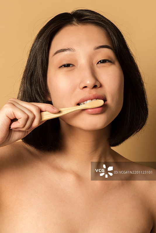 特写肖像：年轻亚洲女性，皮肤光滑，手持牙刷刷牙，面向镜头，摄影棚拍摄。图片素材