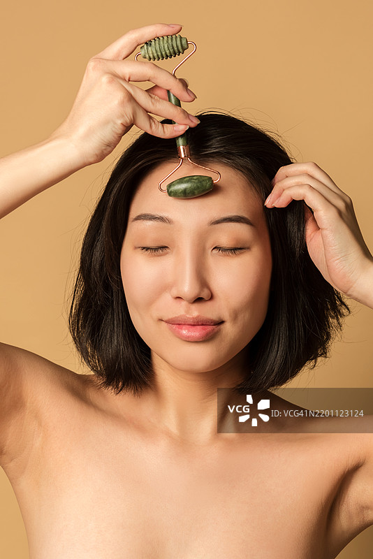 亚洲女性使用滚轮按摩面部肌肤的特写美容肖像图片素材