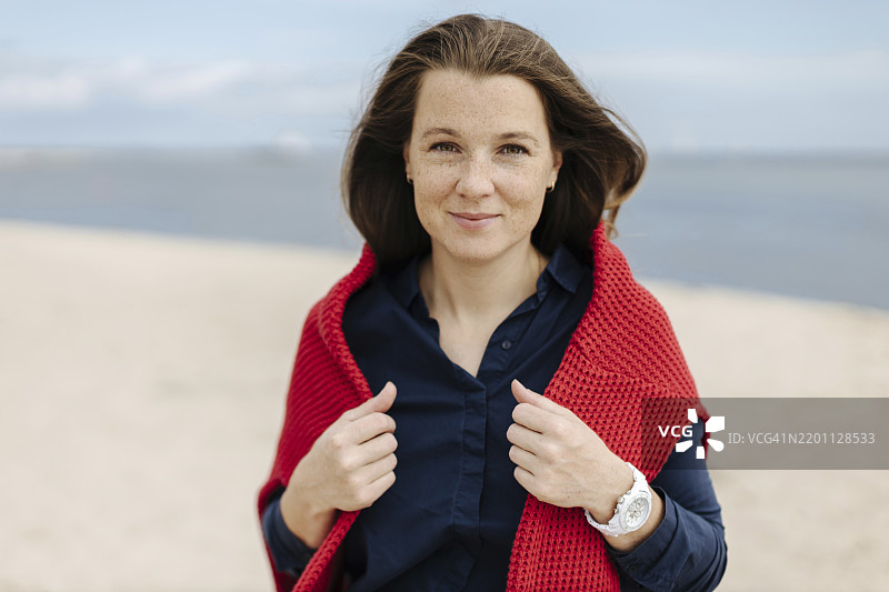 穿着红色针织毛衣的微笑女性在海滩上图片素材