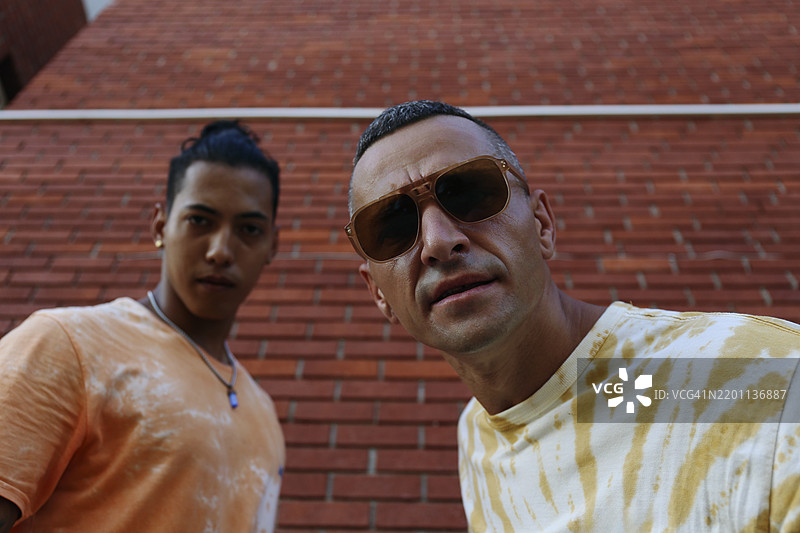 戴着太阳镜的年轻人与兄弟在砖墙旁边图片素材