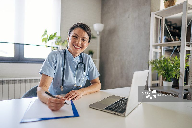女医生在远程医疗预约中微笑并做笔记图片素材