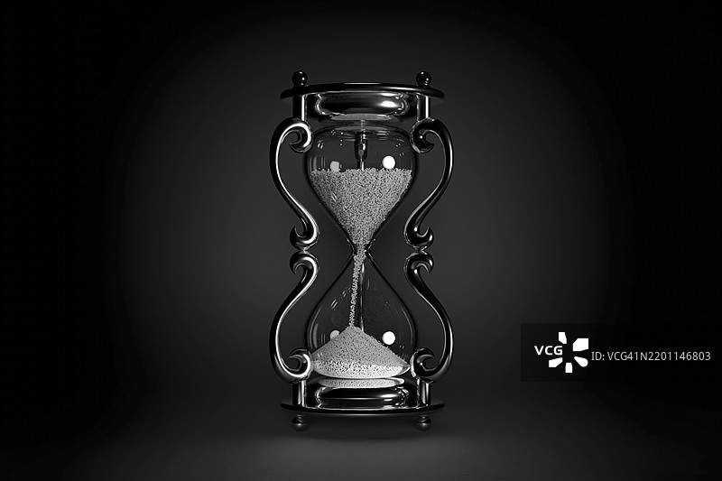 华丽的金属沙漏，里面装有沙子，置于昏暗的工作室环境中图片素材