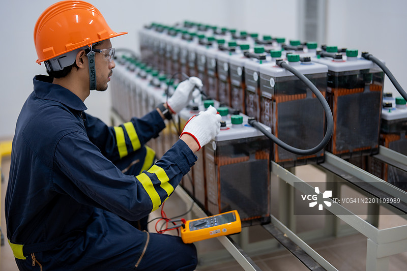 技术人员在工业环境中使用万用表进行电池维护，专注于确保能源存储系统的正常功能和安全性。图片素材