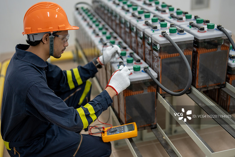 技术人员在工业环境中使用万用表进行电池维护图片素材