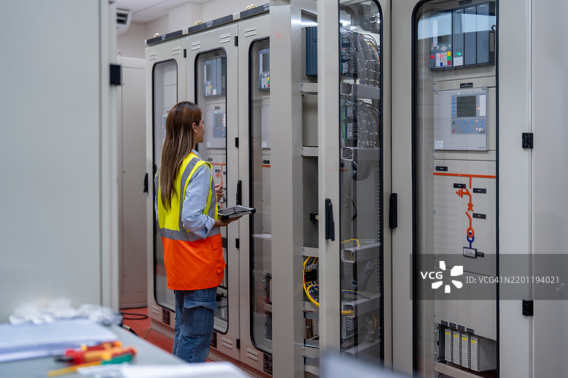 女性电气工程师在设备控制柜检查电气系统，配电变电站中的高压变压器图片素材