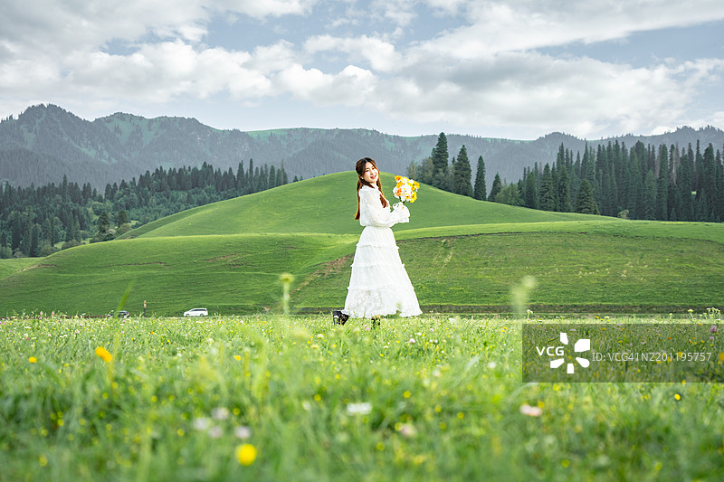 年轻美丽的女子穿着白色波西米亚风格的服装走过草地。图片素材