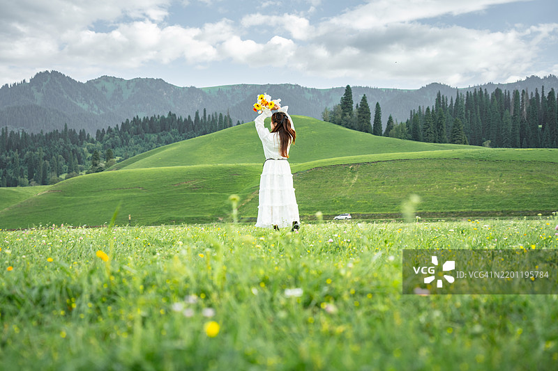 在中国新疆，一位身穿长白裙和草帽的美丽女性正在花海中慢跑，背景是巍峨的山脉。图片素材