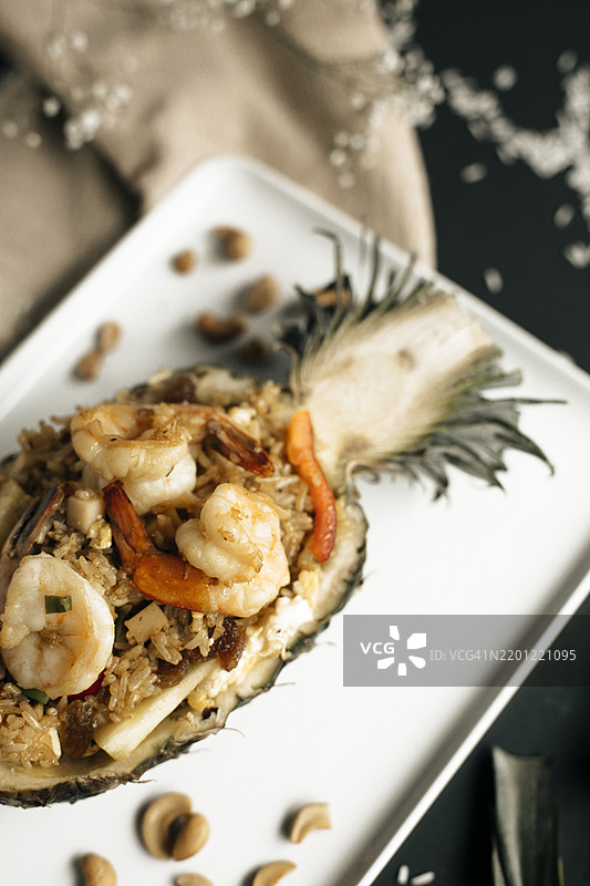 泰式菠萝炒饭（Kao Pad Sapparod），盛放在半个菠萝中，配有虾仁、腰果、蔬菜和米饭，热带风味与异国美食概念，精致的亚洲美食呈现。图片素材