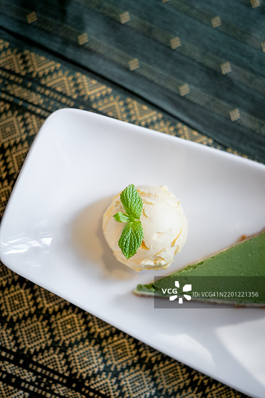 泰式绿茶芝士蛋糕配香草冰淇淋，优雅地摆放在白色盘子上，营造出低调的灯光效果，精致甜点概念图片素材