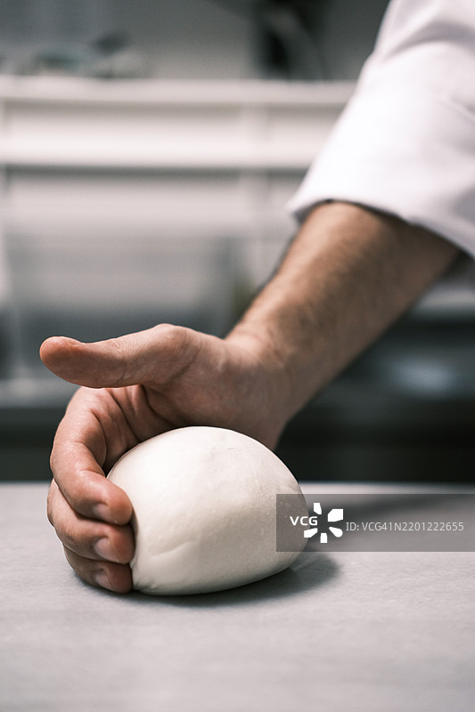 面包师傅在撒了面粉的台面上用手塑形光滑的面团球，专业厨房中的手工面包和比萨面团准备，传统烘焙技巧图片素材