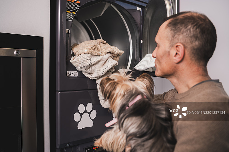 男人在宠物友好的洗衣店照顾他的狗的衣物图片素材