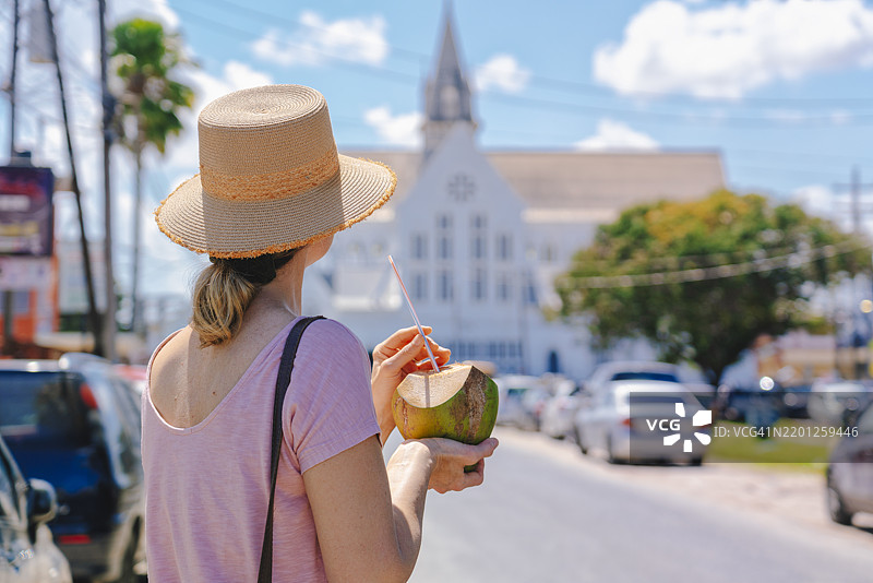 女子在圭亚那乔治城市中心喝椰子水，凝视圣乔治大教堂。图片素材