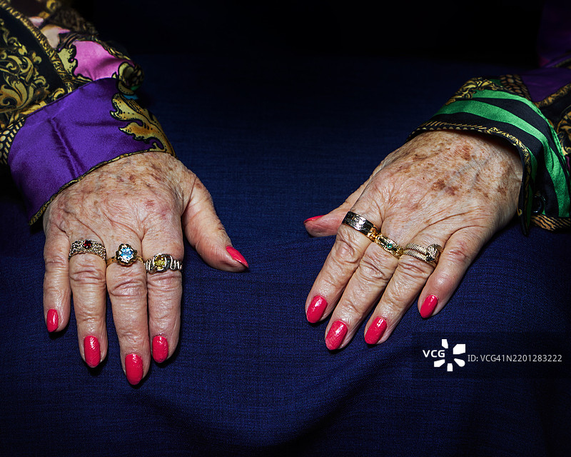 一位老年人的手上佩戴着各种戒指，静静地放在深蓝色的布料上。图片素材