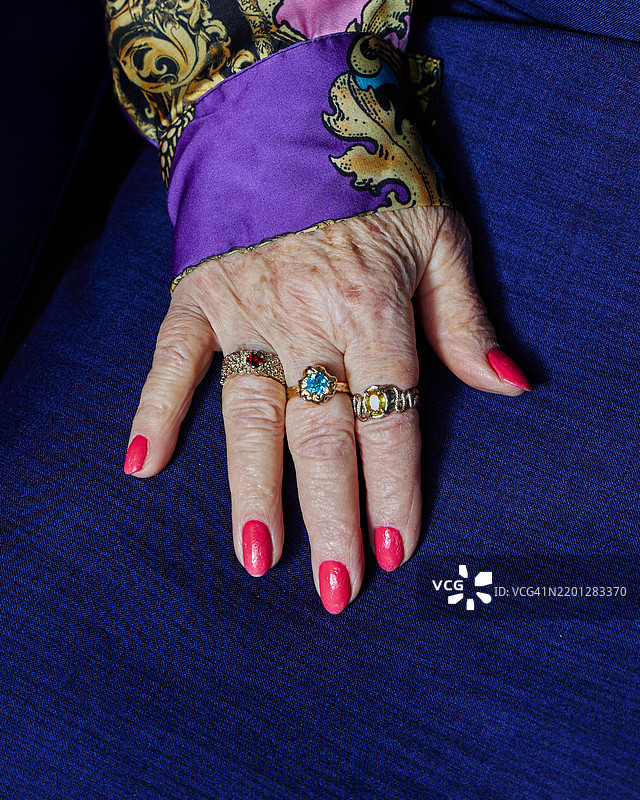 一位老年人的手上佩戴着各种戒指，静静地放在深蓝色的布料上。图片素材