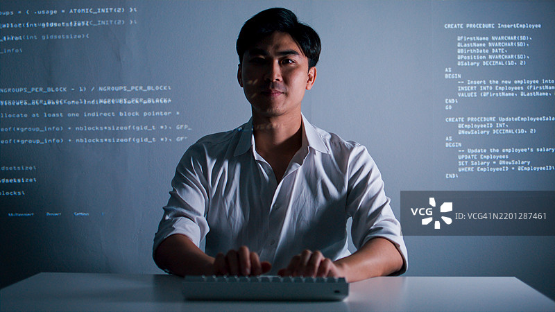 专业的亚洲男性软件开发人员在电脑上编写程序代码，代码行在脸上反射。图片素材