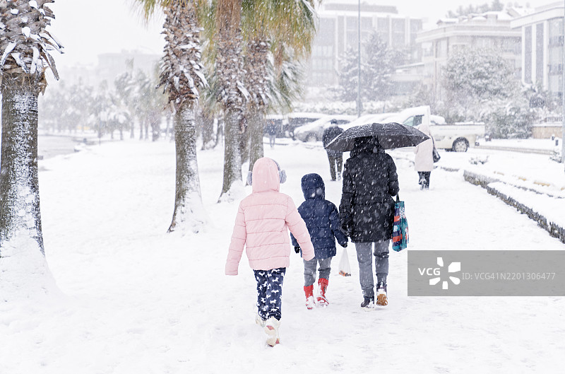 母亲、儿子和女儿在白雪覆盖的道路上走过树枝，沿着暴风雪后的海岸公路。家庭在美丽的冬日里共度时光。图片素材
