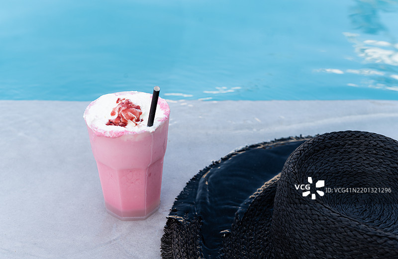 泳池边的粉色奶昔和黑色草帽，享受夏日假期图片素材