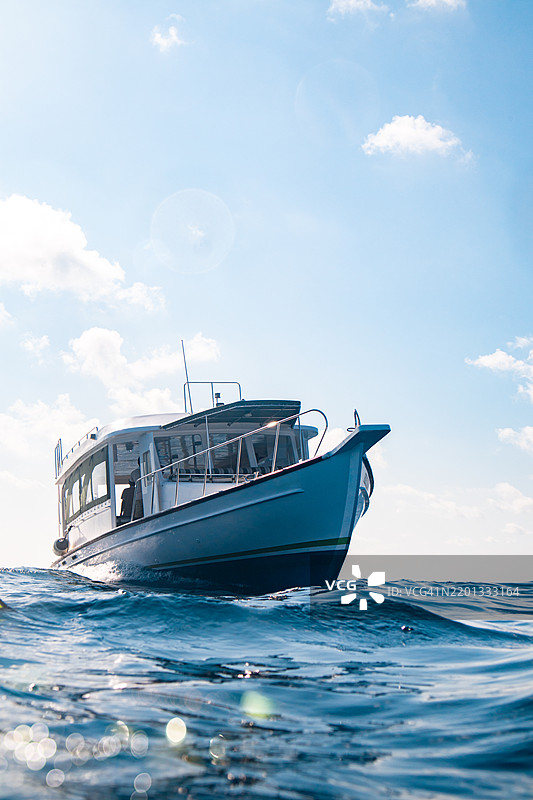 传统马尔代夫多尼潜水船漂浮在碧绿的马尔代夫岛度假村泻湖中，从海面上可以看到正在接送潜水员的场景。图片素材