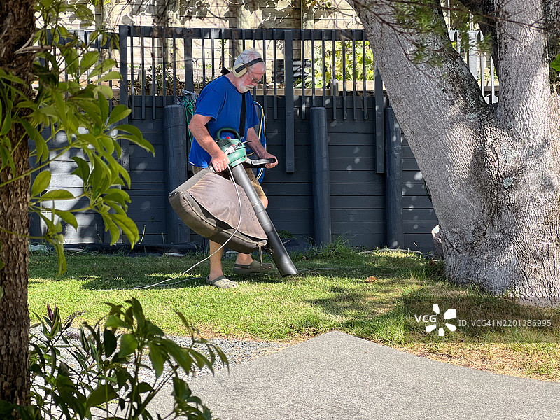 活跃的老年男性在家中的花园里使用落叶吸尘器和粉碎机。图片素材