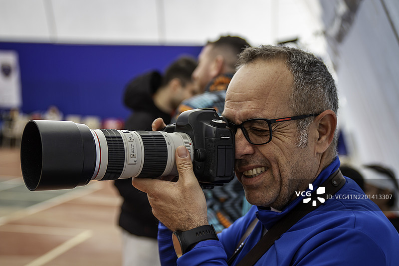 男性摄影师在场地上使用变焦镜头拍摄照片，横向静态画面图片素材