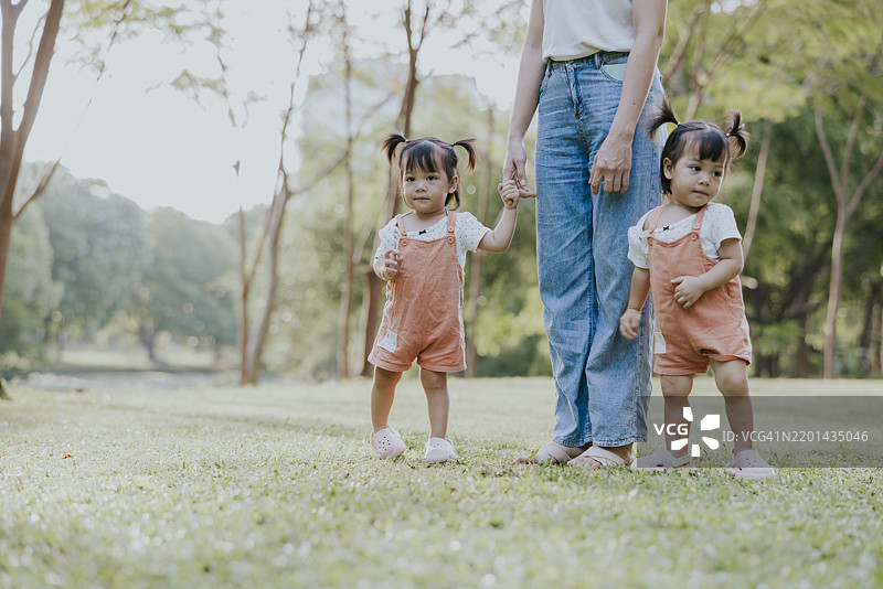 亚洲双胞胎女儿与母亲在公园度假时手牵手散步。图片素材