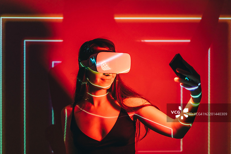 在黑暗中，年轻美丽的女性佩戴虚拟现实眼镜，身上投影出图像。图片素材
