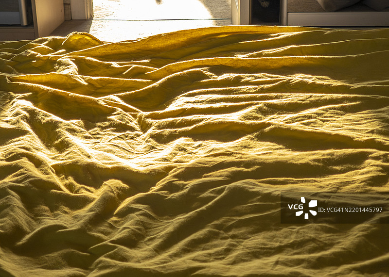 温暖的阳光洒在一条皱褶的黄色毛毯上，营造出一个宁静舒适的房间。图片素材