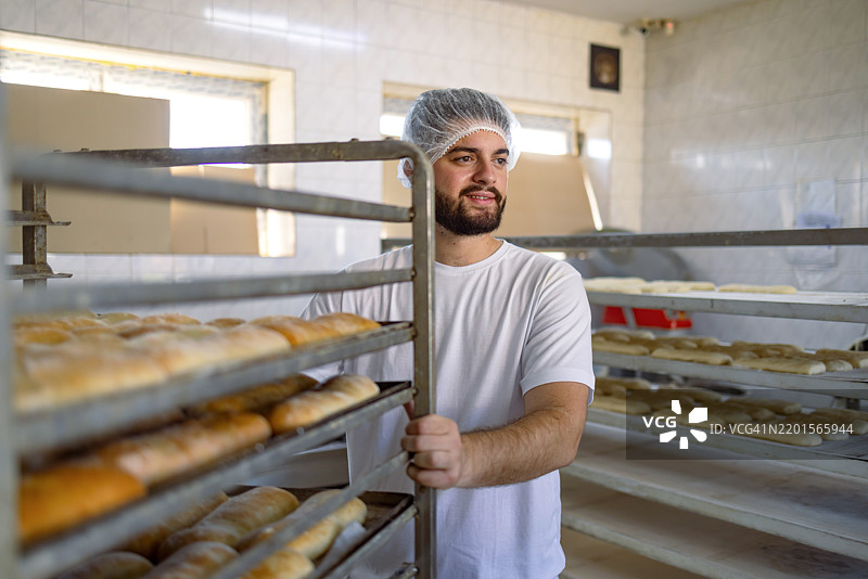 面包师在面包店推着一架新鲜出炉的面包架图片素材