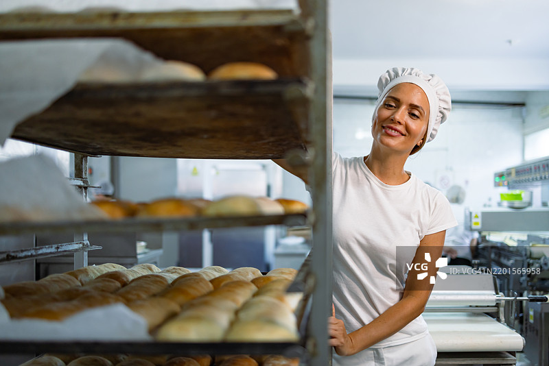 面包师在面包店推着一架新鲜出炉的面包架图片素材