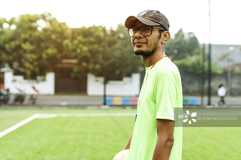 一位足球教练站在足球场上，注视着场地。图片素材