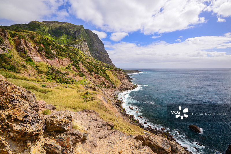 海岸风景，陡峭的悬崖被绿色植被覆盖，向闪耀的蓝色海洋倾斜，天空中点缀着蓬松的云朵。图片素材
