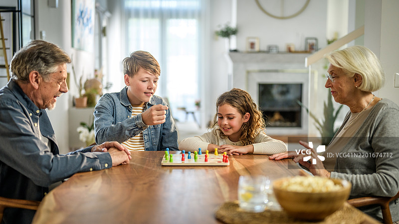 快乐的白人祖父母和孙子孙女在温馨的家中玩飞行棋图片素材