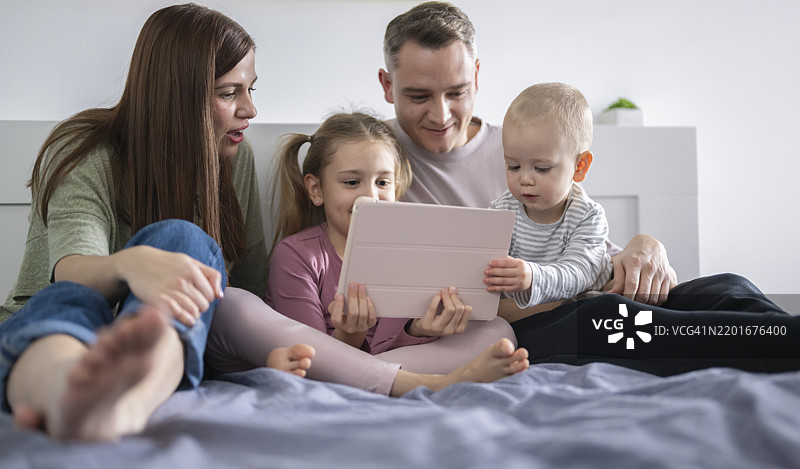 年轻家庭坐在床上专注于电子设备图片素材