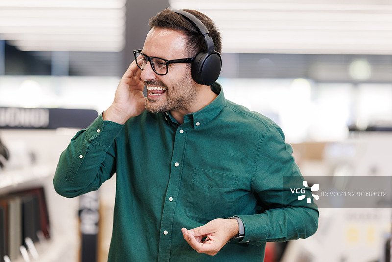 男子在现代电子商店中享受音乐，佩戴无线耳机图片素材