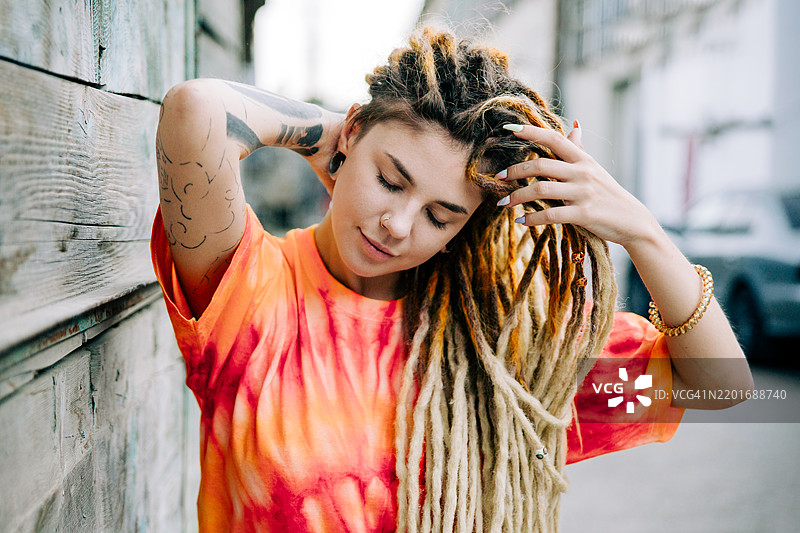 年轻女子，扎着脏辫，身上有纹身，靠在木墙上图片素材
