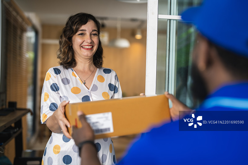 微笑的女性在前门接收快递员送来的包裹图片素材