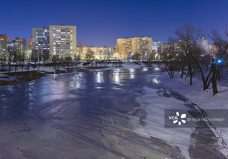 冬季冰冻河流上的宁静黄昏，城市灯光映照在冰冷的水面上图片素材