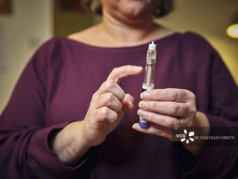 一位女性正在使用赛马鲁肽笔准备进行皮下自我注射。这种现代奇迹的减肥药和糖尿病治疗药物突显了她在家中的个人健康护理日常。图片素材