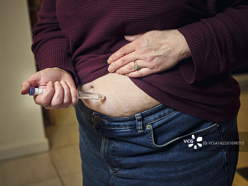一位女性在家中使用半胱氨酸注射笔进行皮下自我注射，这种“减肥药”是现代奇迹般的减重药物和糖尿病治疗药物，突显了个人的健康护理日常。图片素材