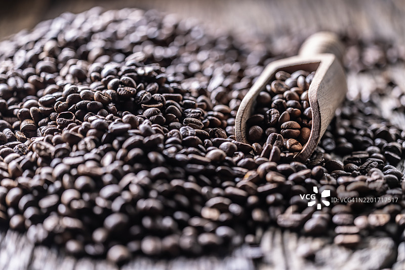 一堆咖啡豆和一个木勺放在一张旧橡木桌上图片素材
