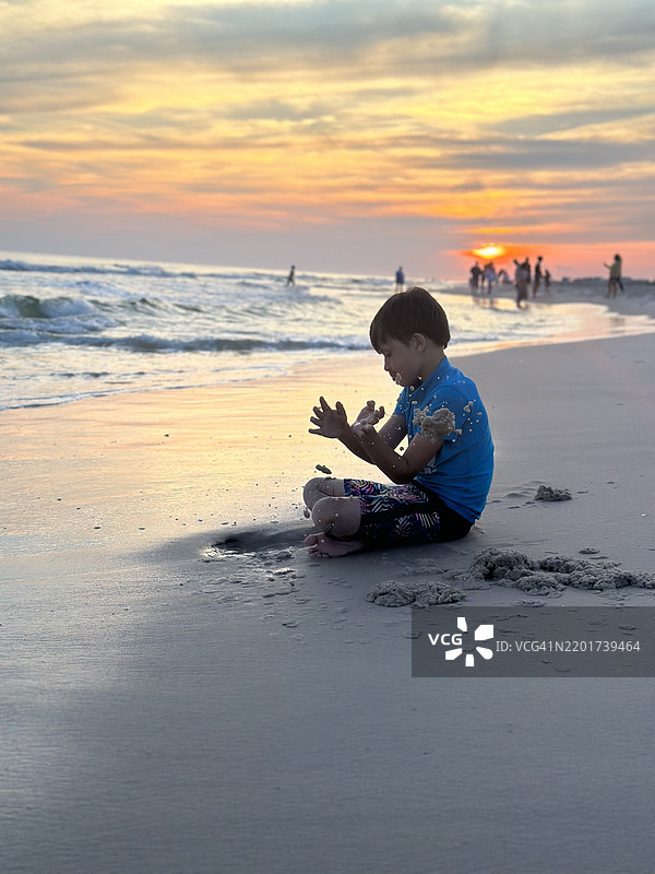 男孩在海滩上玩沙子，侧面视角，背景是日落时分的天空，阿拉巴马州，美国图片素材