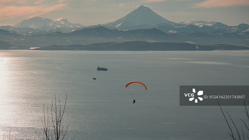 人们在日落时分在海面上空滑翔，背景是山脉。图片素材