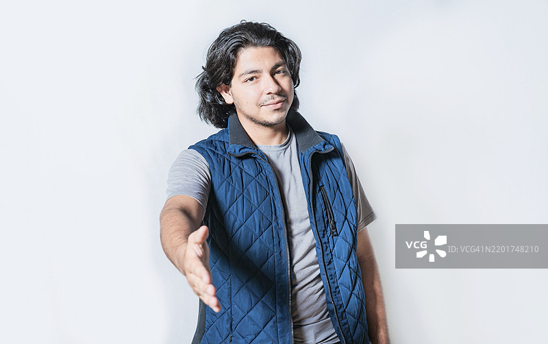 微笑的年轻男子在镜头前挥手，背景干净。友好的年轻男子在镜头前握手，背景干净。图片素材