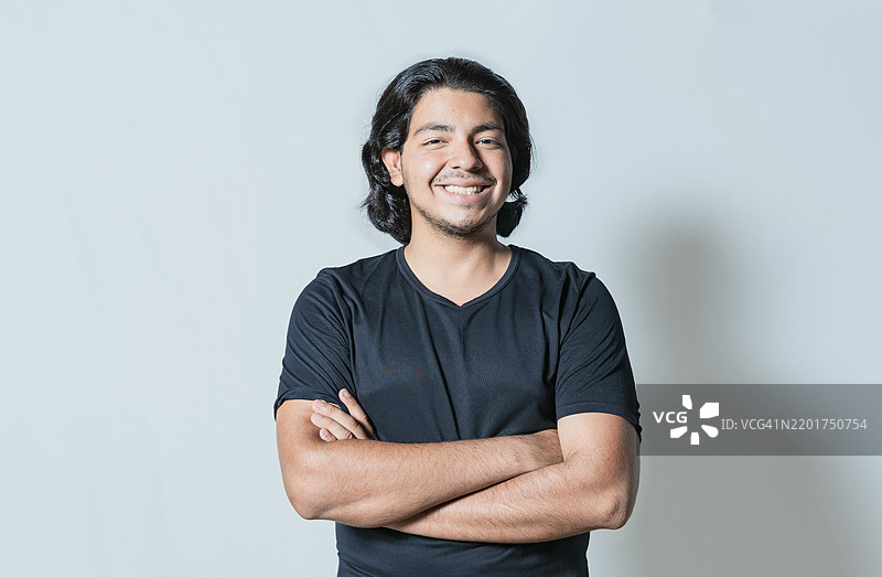 一位英俊的拉丁裔男子双臂交叉，微笑着面对镜头。图片素材