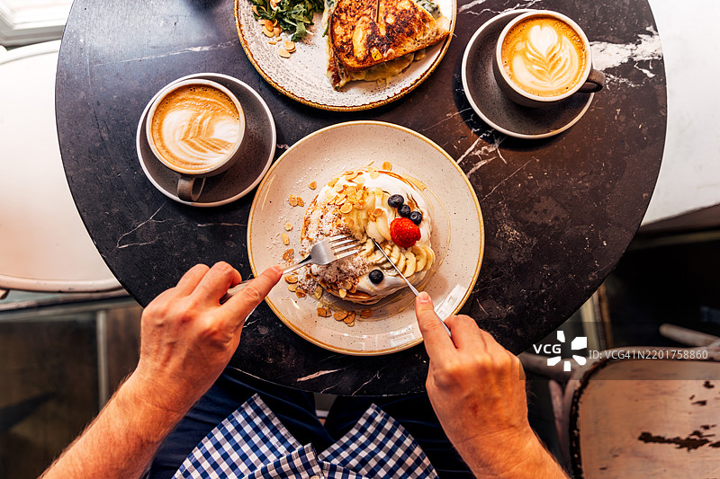 男人在咖啡馆里吃着搭配酸奶和新鲜浆果的煎饼，俯视的个人视角。图片素材